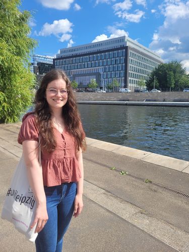 Studentin Julia Antusch mit einem Uni Leipzig-Beutel, im Hintergrund das Gebäude der Bundespressekonferenz